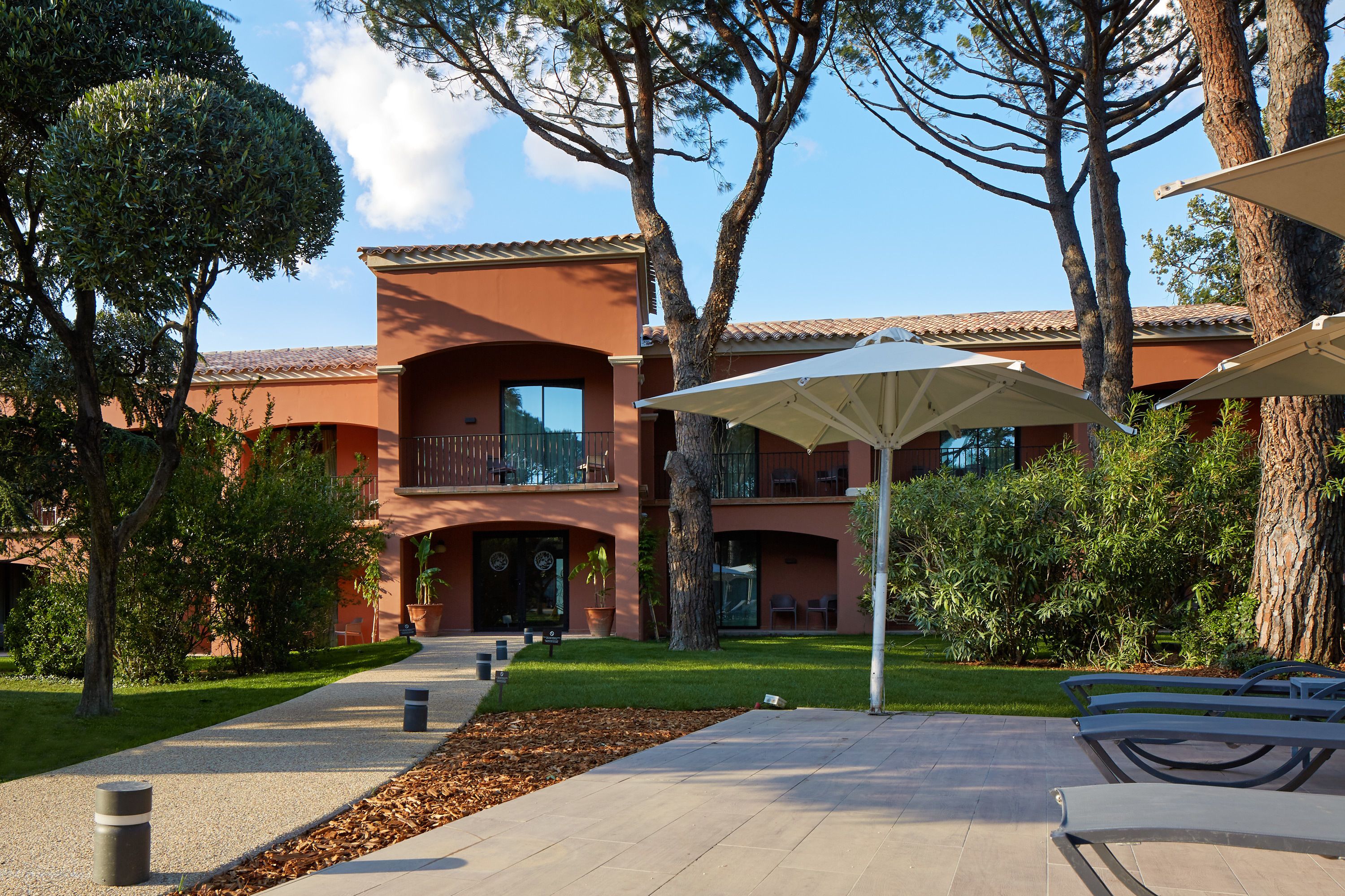 A building with a red facade, large windows, and a covered outdoor seating area with umbrellas.