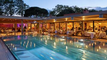 A poolside area with lounge chairs and tables, a bar area with purple lighting, and a restaurant with indoor seating.