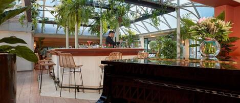A spacious indoor area with a piano, a bar, and a seating area with chairs and tables.