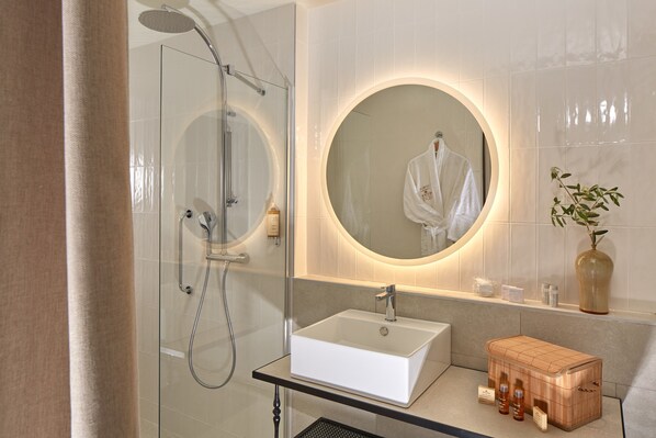 A modern bathroom with a glass-enclosed shower, a white sink, and a round mirror.