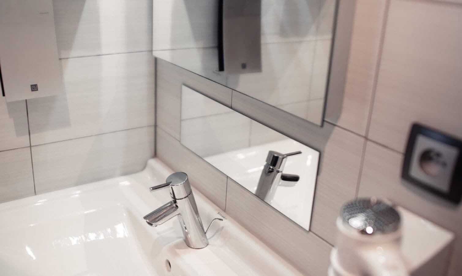 Un baño moderno con lavamanos blanco, grifo cromado y espejo encima.