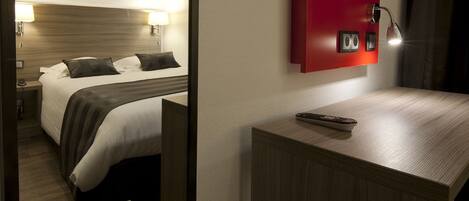 Habitación de hotel con cama, lámparas de noche, un espejo, una pared de acento roja y una mesita de noche con control remoto.
