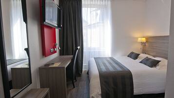 Une chambre d’hôtel avec un lit, un bureau, une télévision et une fenêtre avec des rideaux.