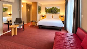 Une chambre d’hôtel avec un lit, un canapé rouge, une petite table, une chaise et un miroir.