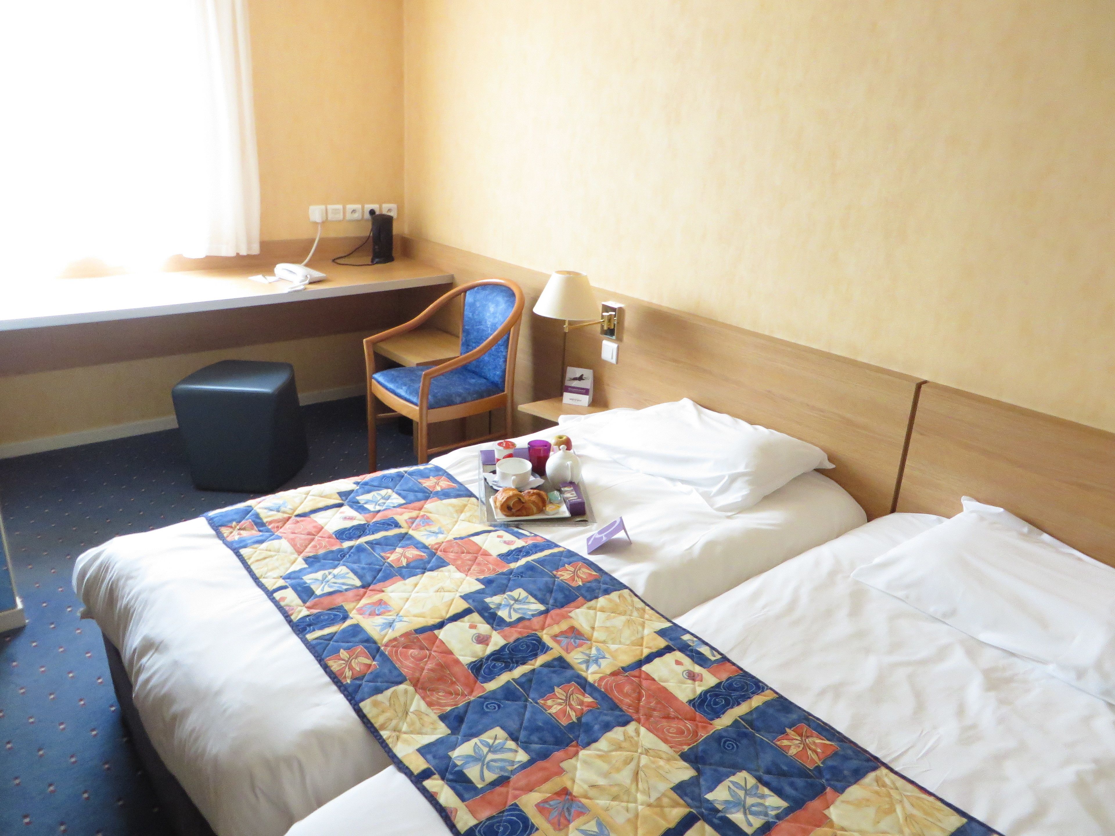 Ein Hotelzimmer mit einem Bett, einem Schreibtisch, einem Stuhl und einem kleinen Hocker.