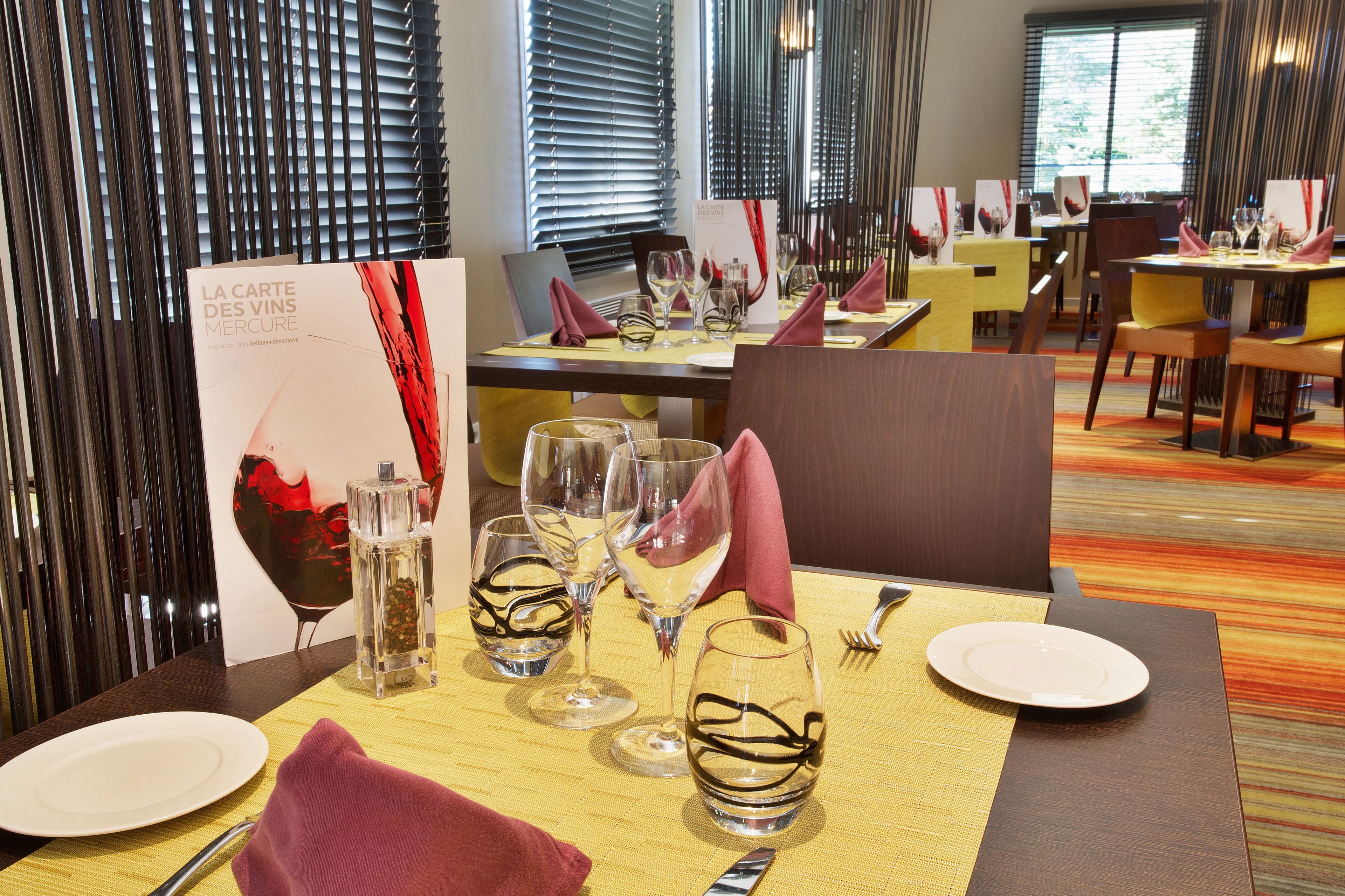 A dining area with tables set for a meal, featuring wine glasses, plates, and cutlery.