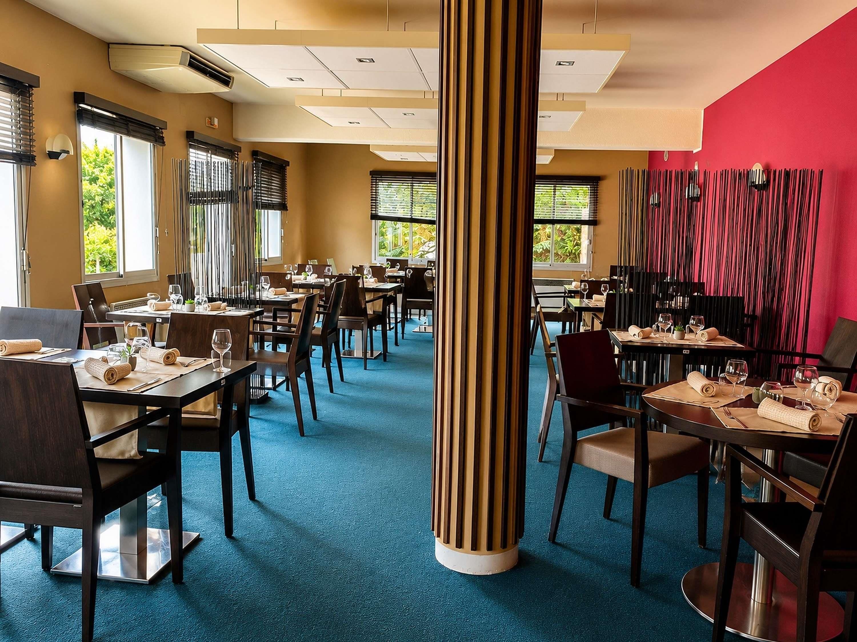 Een restaurant met meerdere tafels en stoelen, een blauw vloerkleed en een rode accentmuur.