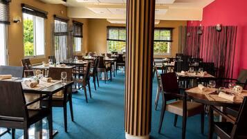 Een restaurant met meerdere tafels en stoelen, een blauw vloerkleed en een rode accentmuur.