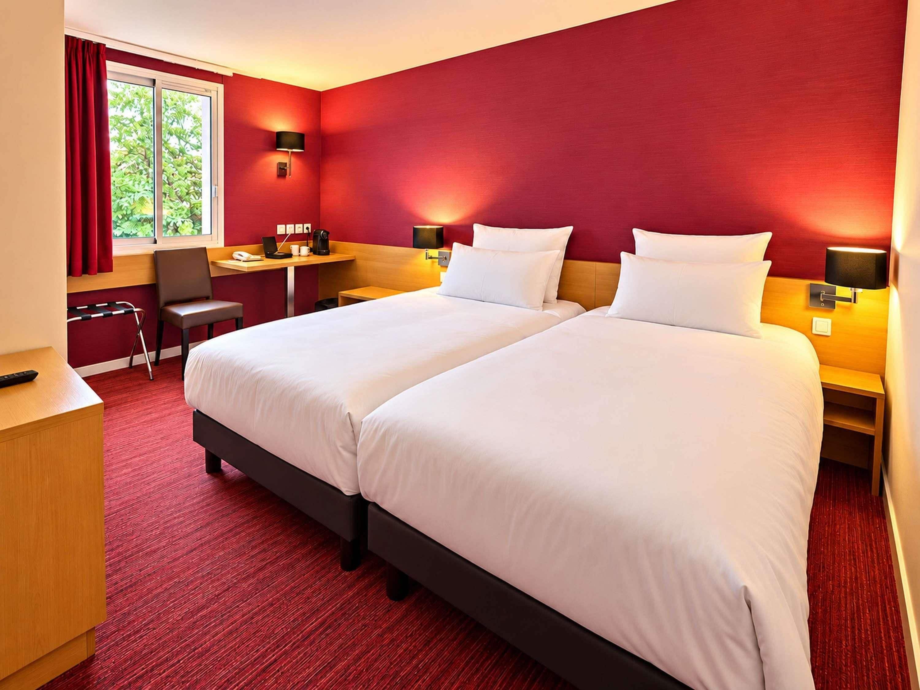 Quarto de hotel com duas camas, uma mesa, uma cadeira e uma janela com cortinas.
