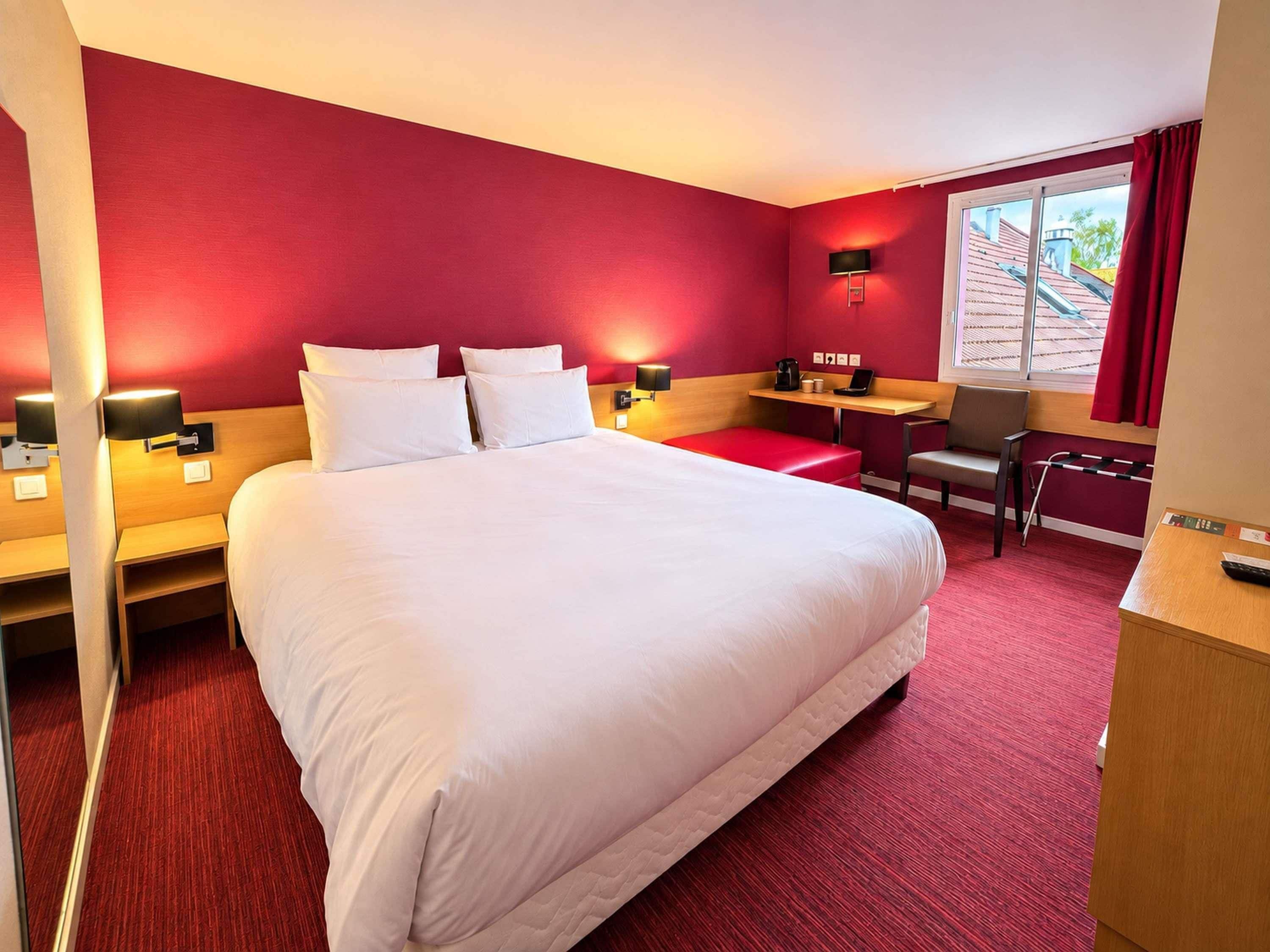 Une chambre d’hôtel avec un grand lit, un bureau, une chaise et une fenêtre avec des rideaux.