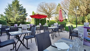 An outdoor dining area with tables and chairs, surrounded by trees and a clear sky. - Mercure Luxeuil les Bains Hexagone (Luxeuil-les-Bains)
