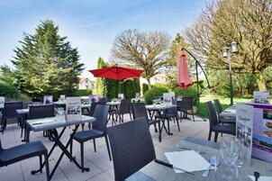 Un espace extérieur aménagé pour les repas, avec des tables et des chaises, entouré d’arbres et sous un ciel dégagé.
