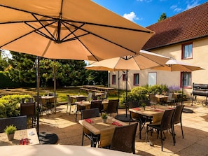 An outdoor patio with tables and chairs, umbrellas, and a barbecue grill.