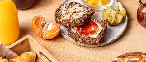 Desayuno con tostadas, fruta y cruasanes sobre una mesa de madera.