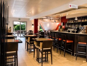 Ein Restaurantinneres mit Tischen und Stühlen, ein Barbereich mit Flaschen und einer Kasse, und ein Schild, das eine Brasserie kennzeichnet.