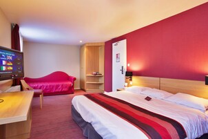 Habitación de hotel con cama, escritorio, televisor, sofá rojo y armario de madera.