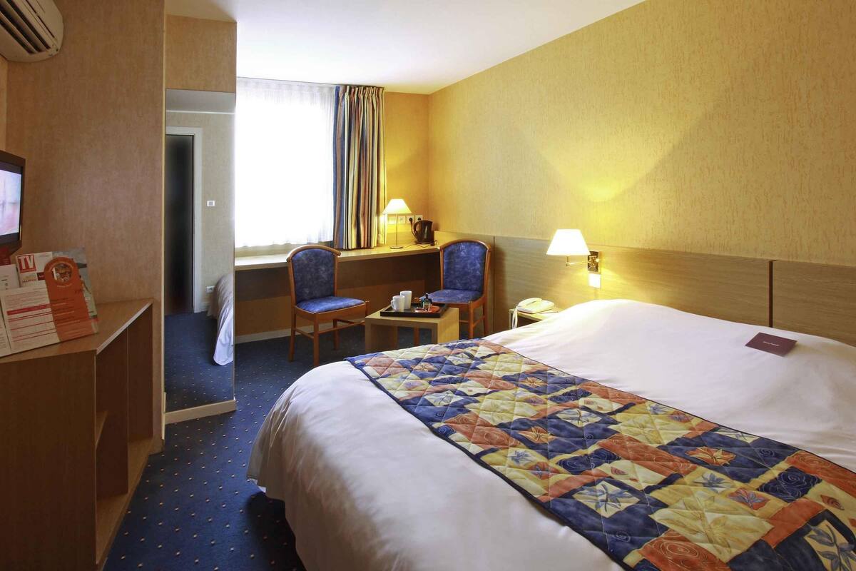 A hotel room with a large bed, a desk with a chair, a TV, and a window with curtains.