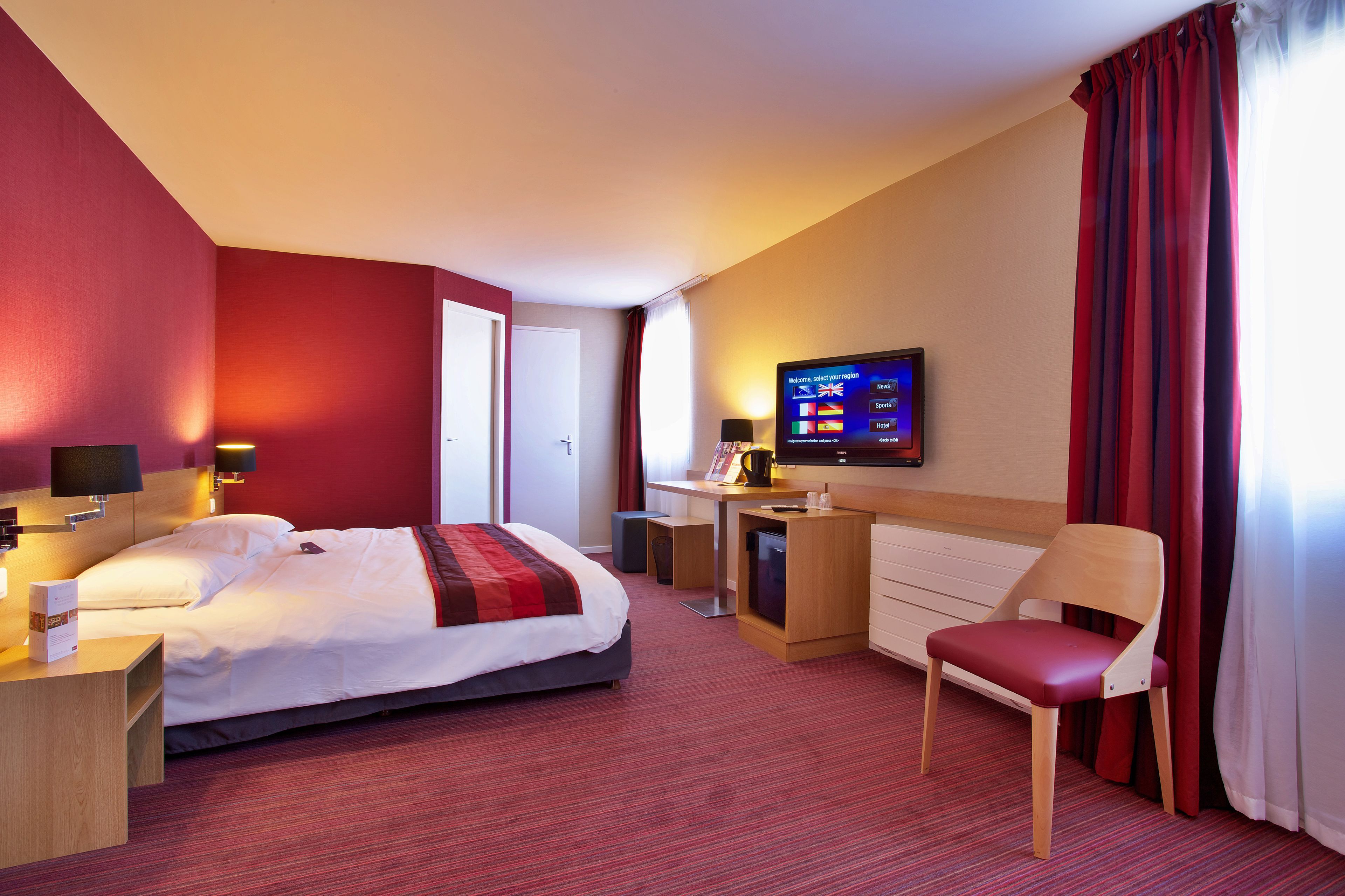 A hotel room with a bed, desk, chair, TV, and curtains.