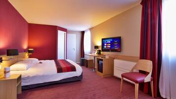 A hotel room with a bed, desk, chair, TV, and curtains.