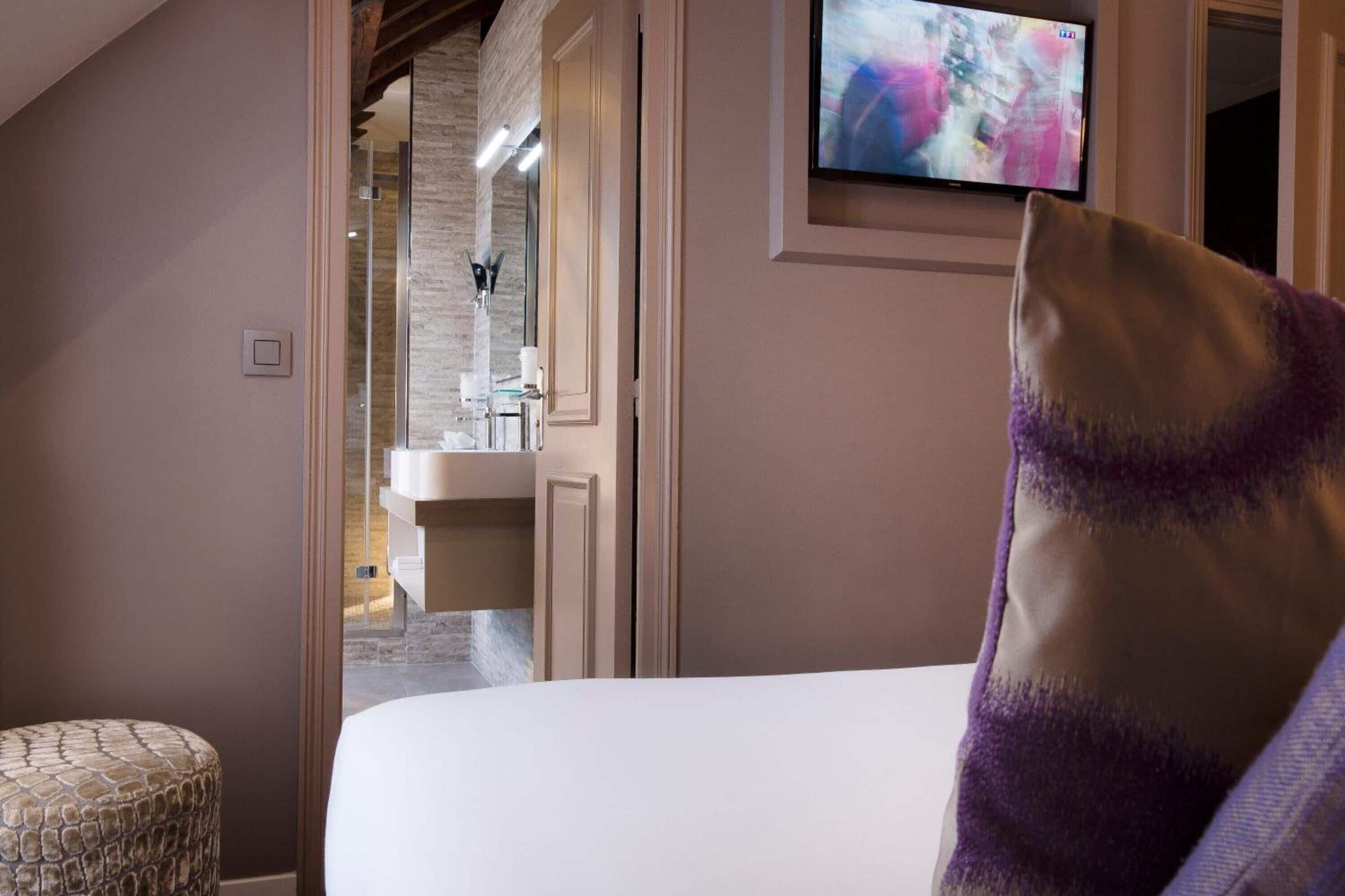 Ein Hotelzimmer mit einem Bett, einem an der Wand befestigten Fernseher und einem durchgegangenen Tür erkennbaren Badezimmer.