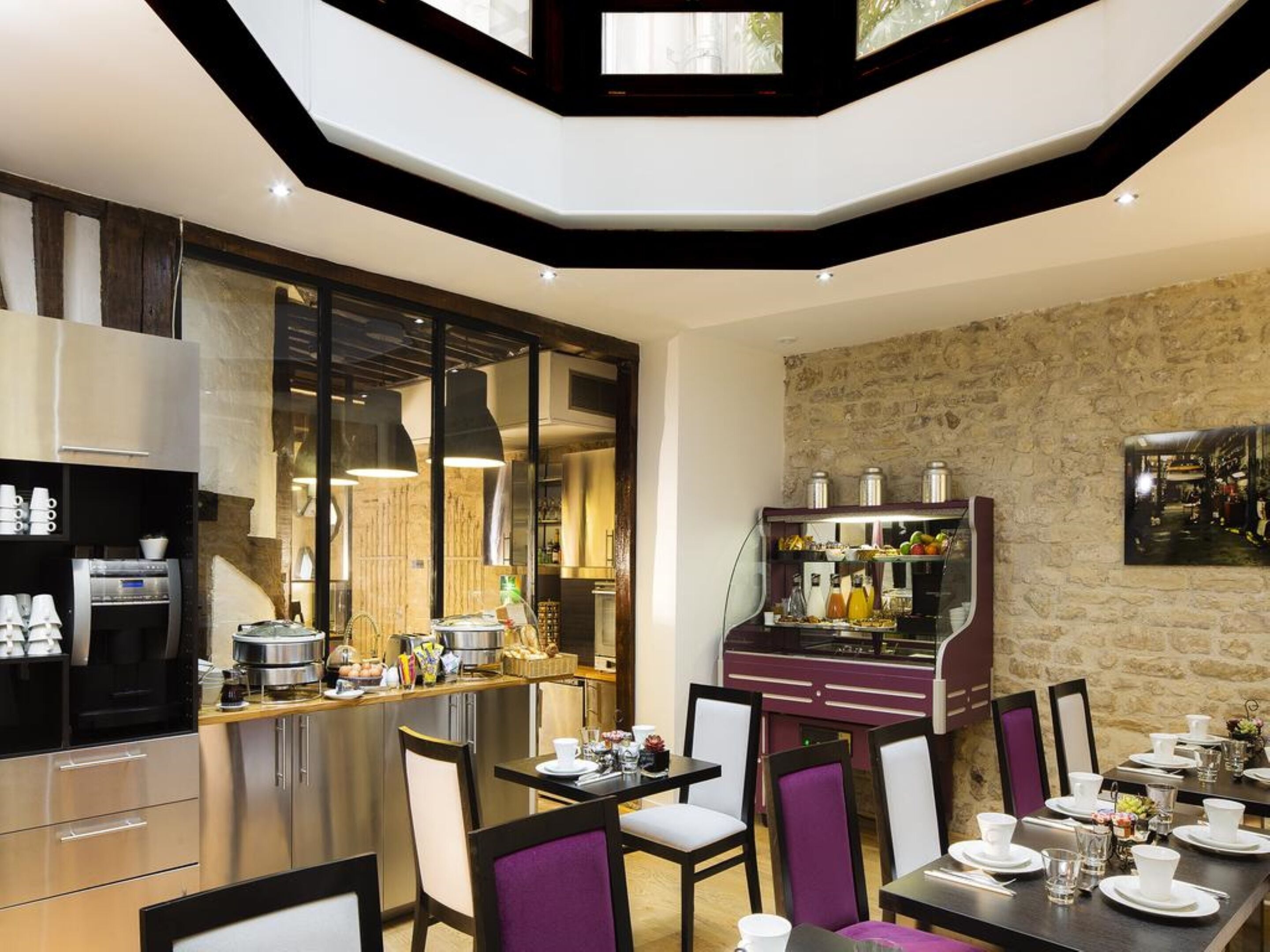 A modern dining area with a kitchen in the background, featuring stainless steel appliances and a stone wall.