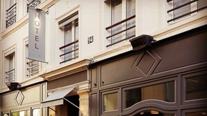 La façade d’un hôtel, avec de grandes fenêtres, une enseigne bien visible indiquant « HÔTEL » et le chiffre « 94 » au-dessus de l’entrée.