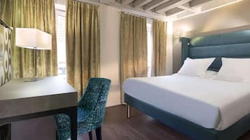 A hotel room with a bed, a desk, a chair, and curtains.