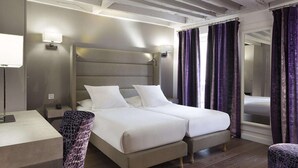 Une chambre avec un lit double doté d’une tête de lit, de tables de chevet, d’un bureau et d’une chaise, et dont le plafond est orné de poutres en bois.