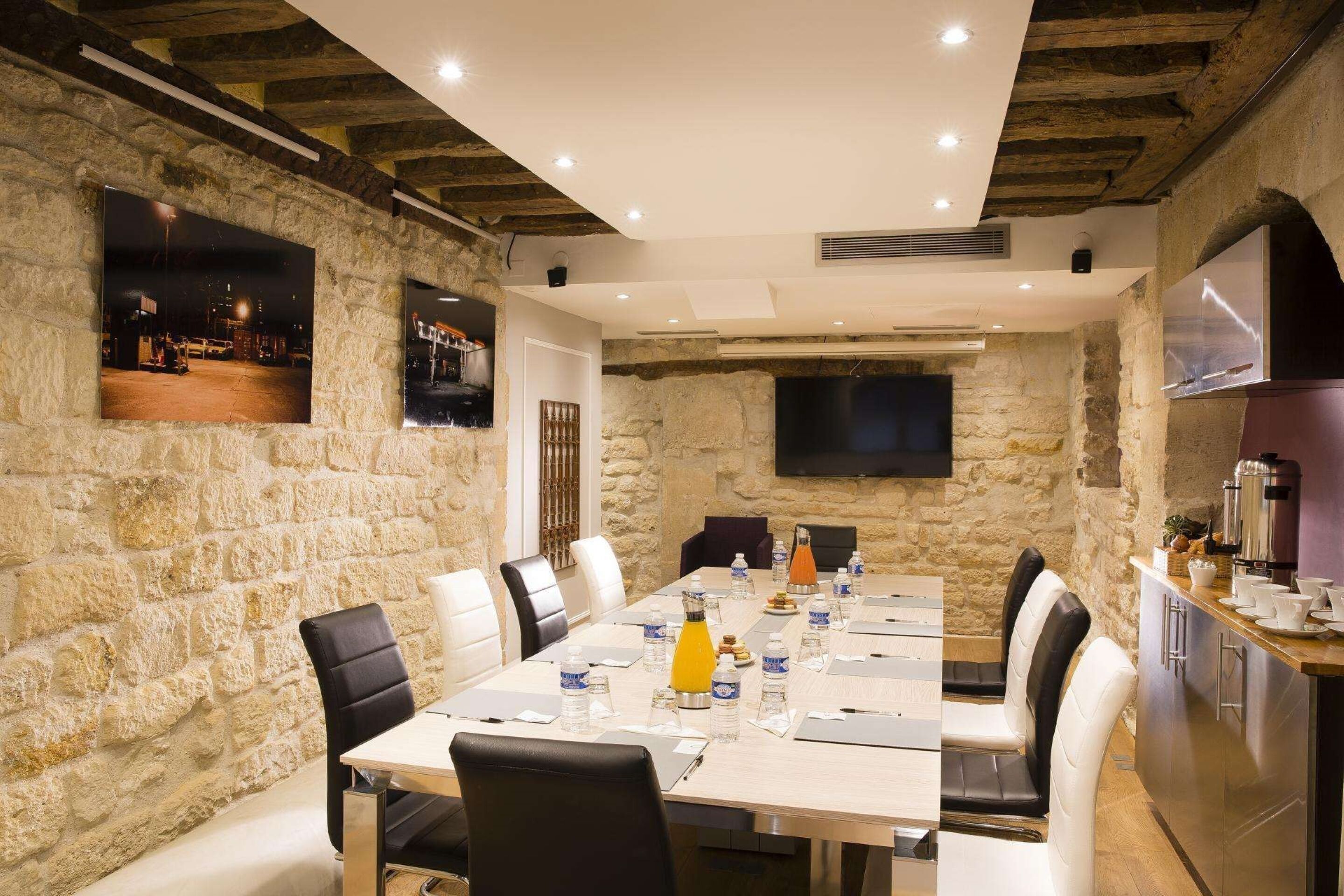 A conference room with a stone wall, a long table with chairs, and a flat-screen TV mounted on the wall.