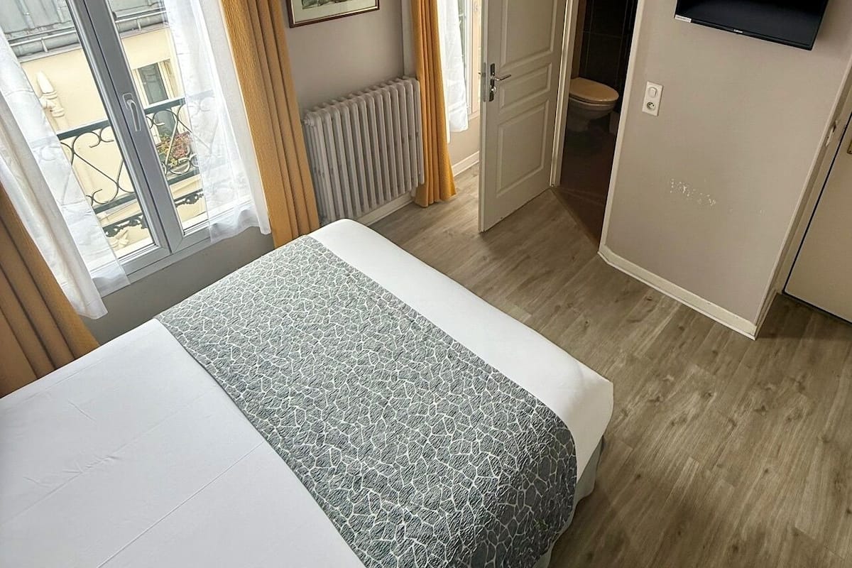 A hotel room with two beds, a radiator, a TV, and a window with curtains.