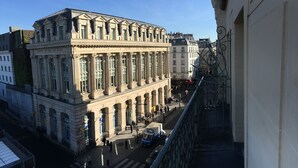 Un grande edificio in stile classico con colonne e un ingresso centrale, circondato da una strada trafficata con pedoni e veicoli.