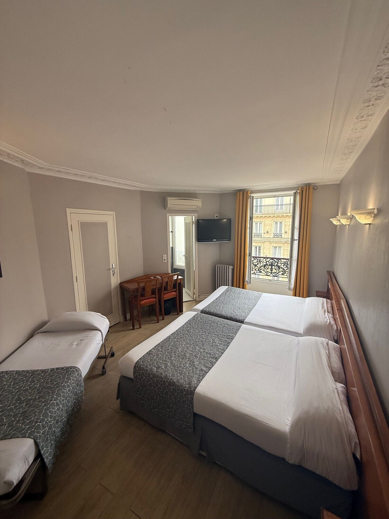 Ein Hotelzimmer mit zwei Einzelbetten, einem Doppelbett, einem Holztisch, einem Stuhl, einem Fernseher und einem Fenster mit Vorhängen.
