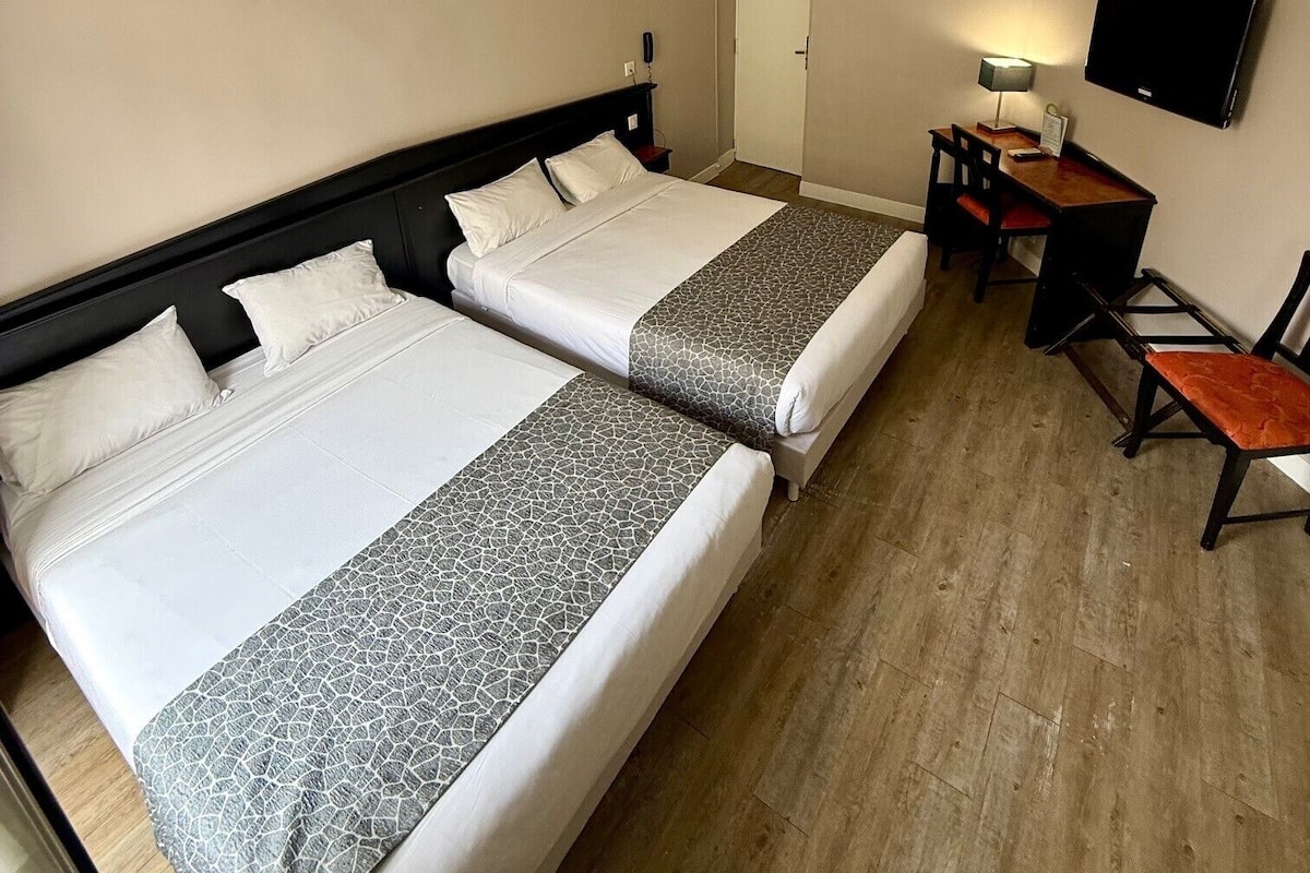 A hotel room with two beds, a desk, a chair, a television, and a door.