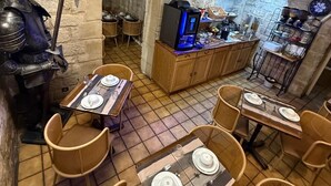 Un interno rustico con pareti in pietra, un arco in pietra, un tavolo in legno apparecchiato per due, sedie in vimini e un angolo cottura con un elettrodomestico moderno.