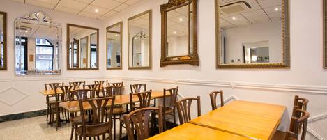 A dining area with multiple wooden tables and chairs, large mirrors on the walls, and a tiled ceiling.
