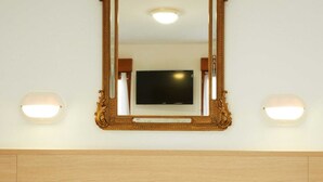 A hotel room with a large ornate mirror above a bed, two bedside lamps, and a flat-screen TV mounted on the wall. - Hôtel Darcet Paris (Paris)