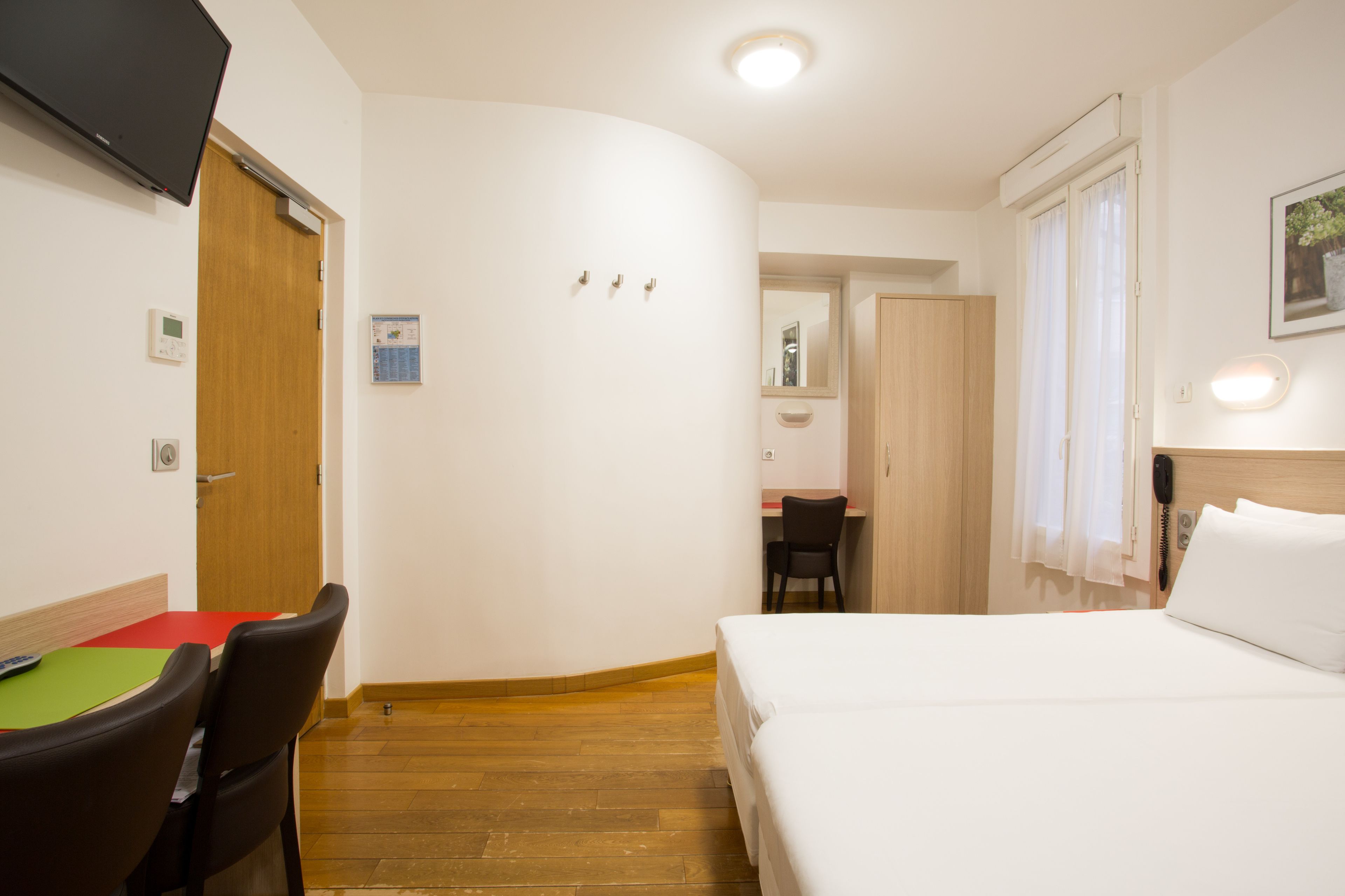 A hotel room with a bed, a desk with a chair, a television, and a wooden floor.