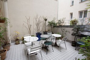 A tiled patio with metal tables and chairs, surrounded by potted plants and a low wall. - Hôtel Darcet Paris (Paris)