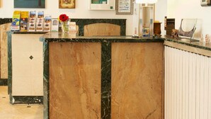 A hotel reception area with a marble counter, a reception desk, a framed picture, a lamp, and a wall-mounted screen. - Hôtel Darcet Paris (Paris)