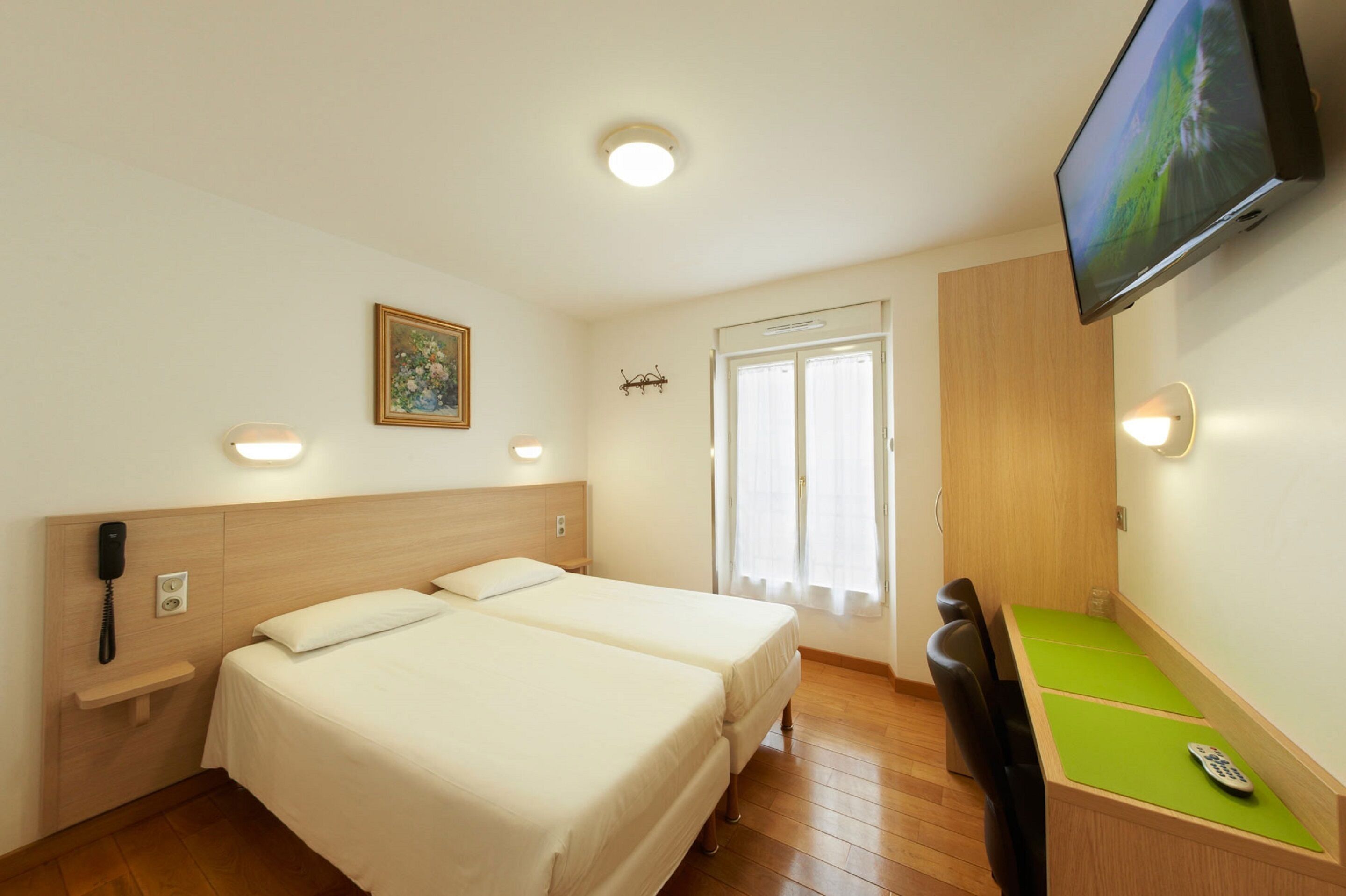 A hotel room with two beds, a desk, a chair, a TV, and a phone on the wall.