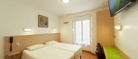 A hotel room with two beds, a desk, a chair, a TV, and a phone on the wall.