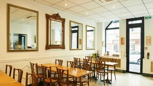 A dining area with wooden tables and chairs, large mirrors on the walls, and a view of the street through a door. - Hôtel Darcet Paris (Paris)