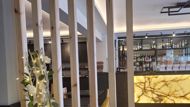 Un comptoir d’accueil avec un menu, un bar avec des étagères remplies de bouteilles et une plante décorative.