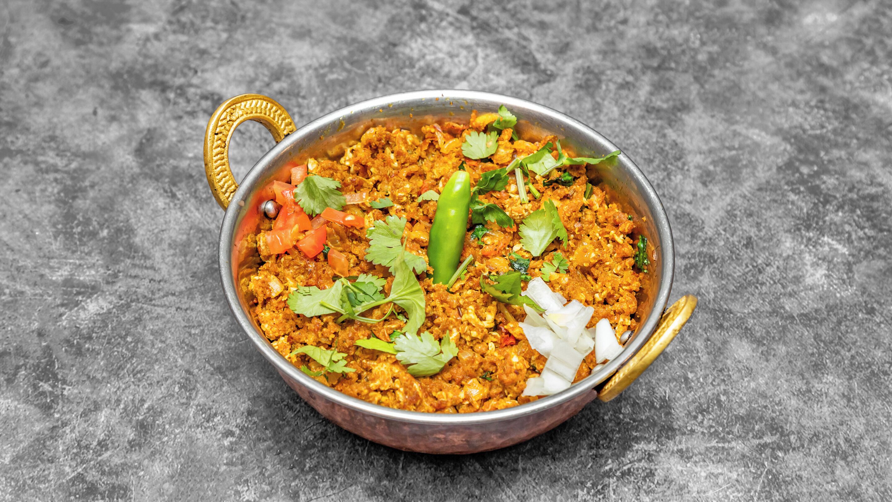 A bowl of food with a handle, garnished with cilantro and a green chili, on a textured surface.