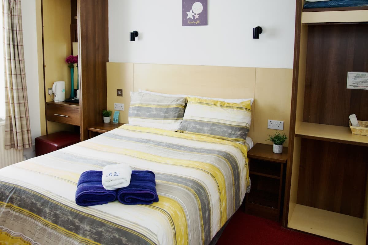 A hotel room with a bed, a nightstand, a wardrobe, and a window with curtains.
