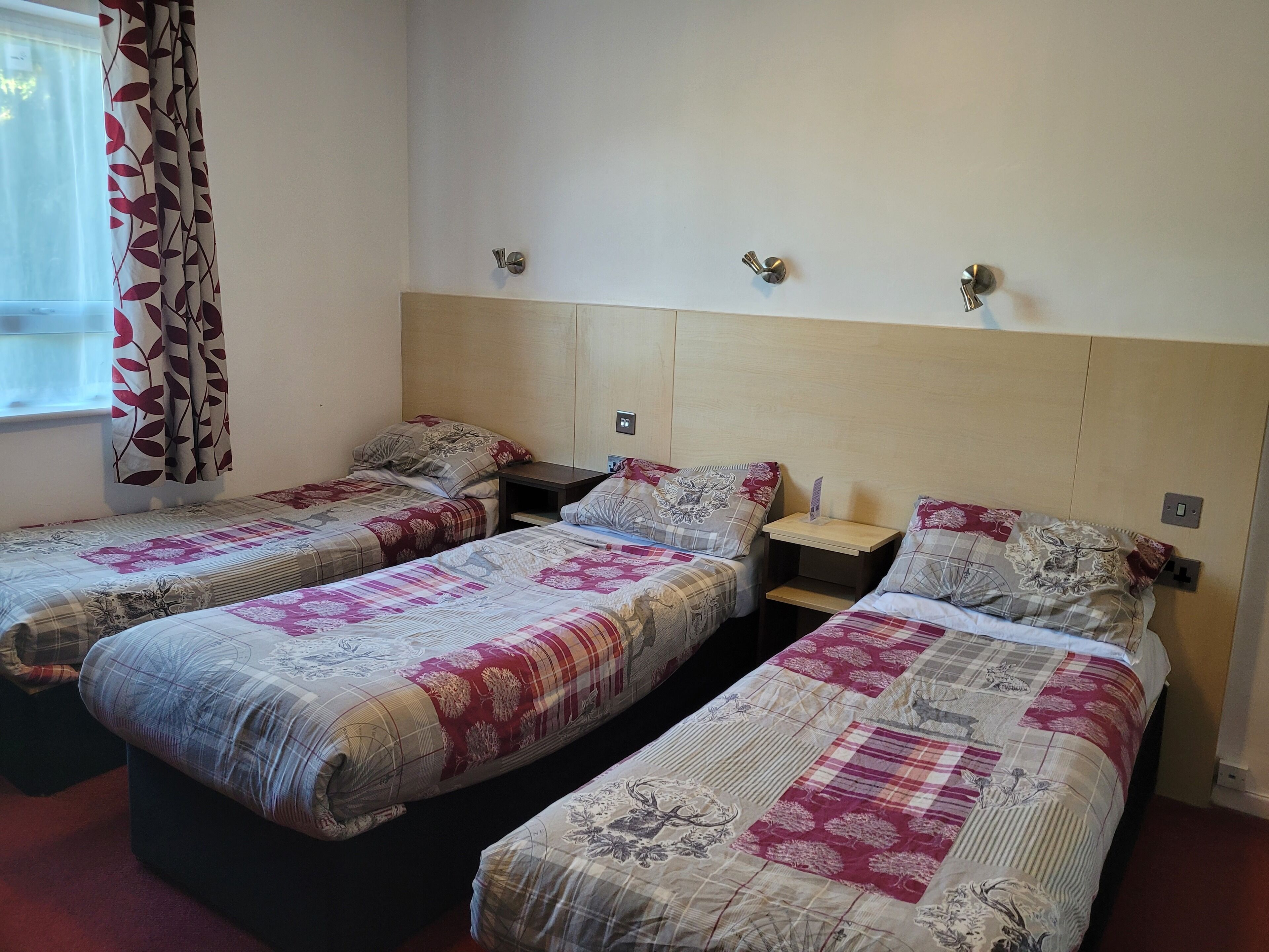 A hotel room with two single beds, each with floral-patterned bedding, a wooden headboard, and bedside tables with lamps.