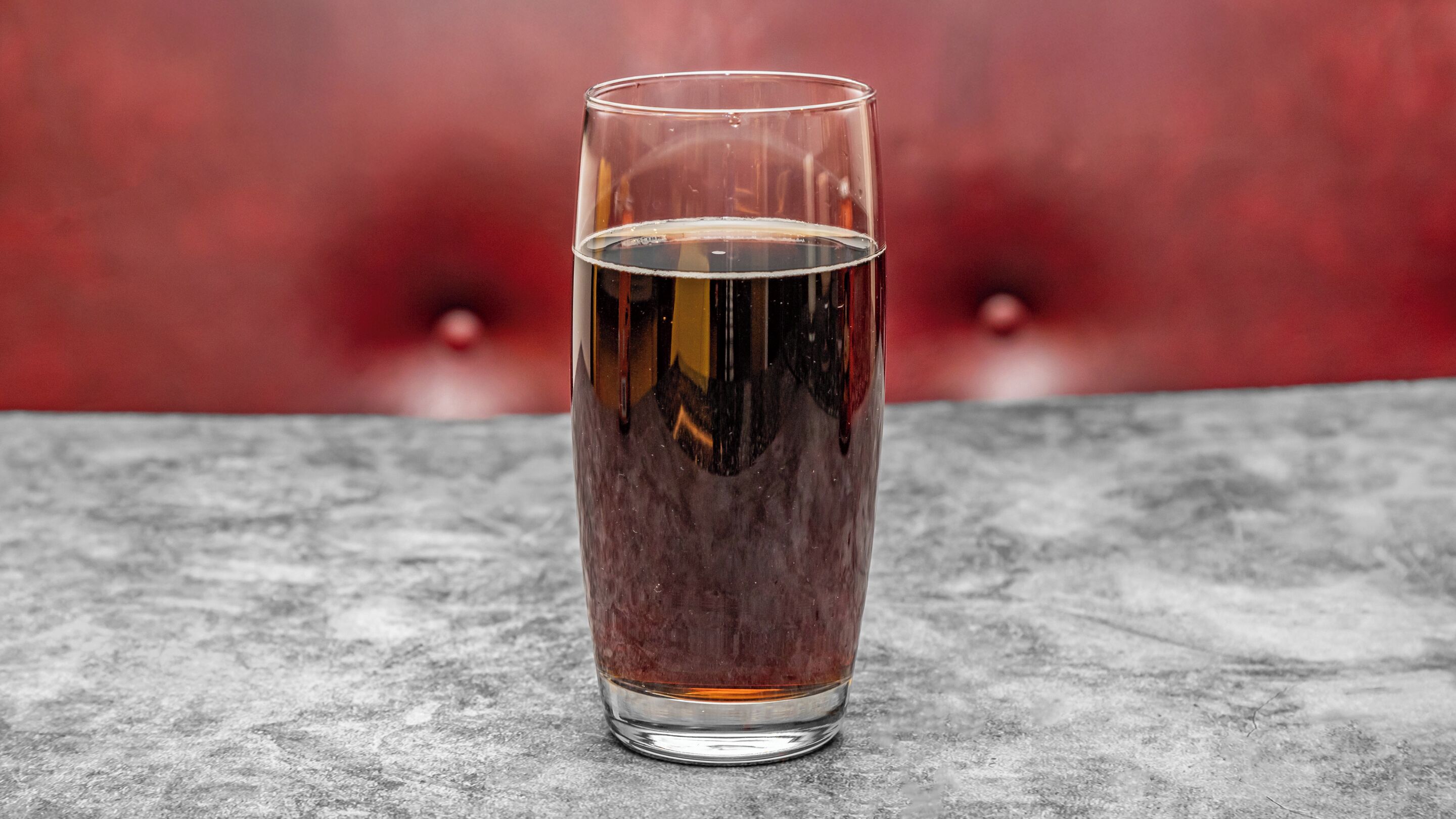 A tall glass of amber liquid on a textured surface.