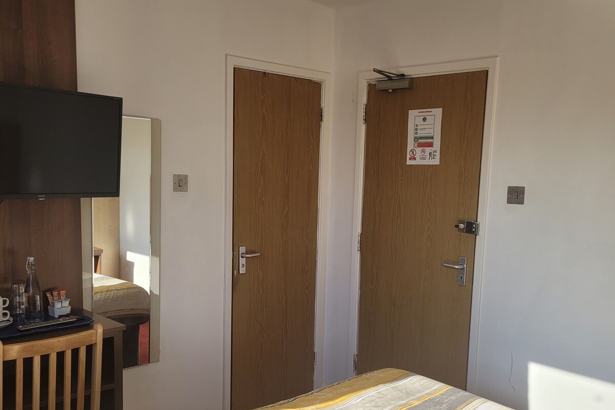Une chambre à coucher avec un lit, un téléviseur fixé au mur et deux portes.