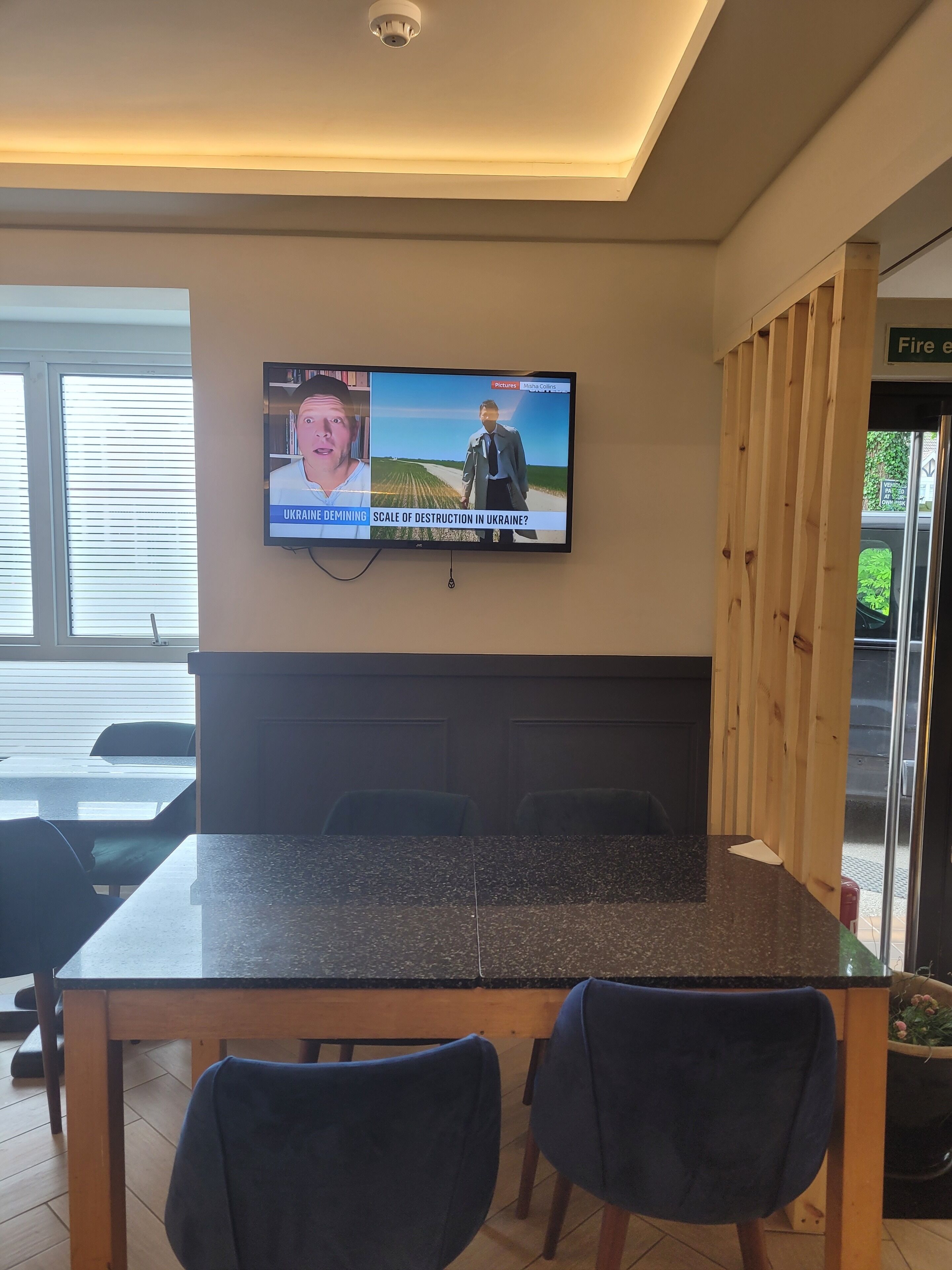 A modern kitchen with a granite countertop, two dark chairs, and a television displaying news about Ukraine.