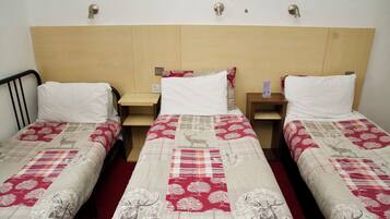 A hotel room with three single beds, each with a red and white patterned bedspread. There are wooden headboards and nightstands between the beds.